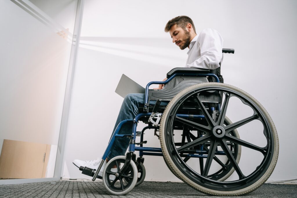 Man in wheelchair using laptop in office hallway.