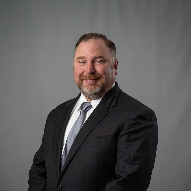 Professional headshot of Steven Gensemer, Esq., smiling, wearing a dark suit with silver tie, against a gray background.