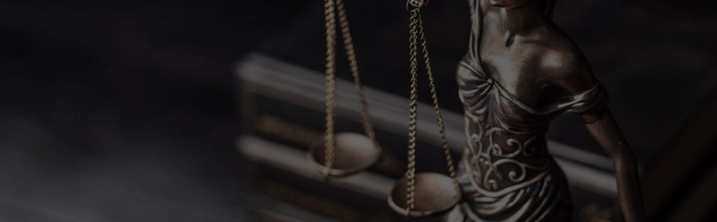 Statue of Lady Justice holding scales, dramatically lit against dark background.