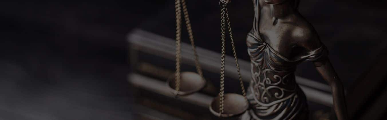 Statue of Lady Justice holding scales, dramatically lit against dark background.