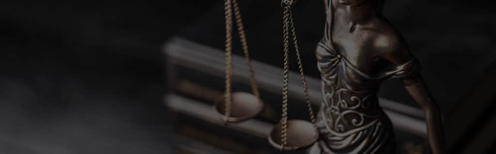 Statue of Lady Justice holding scales, dramatically lit against dark background.