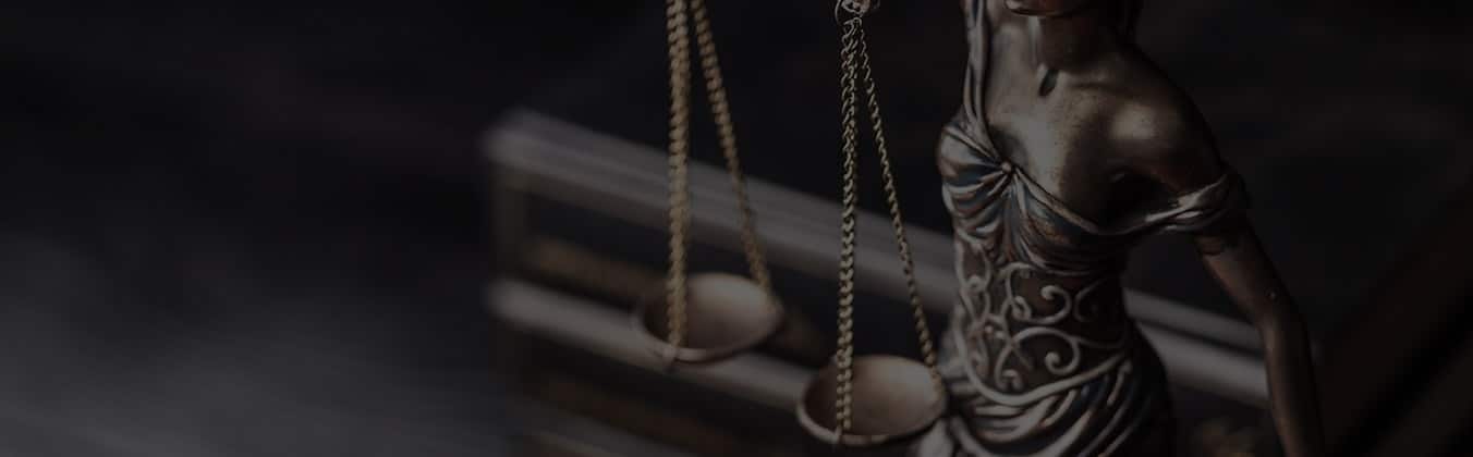 Statue of Lady Justice holding scales, dramatically lit against dark background.