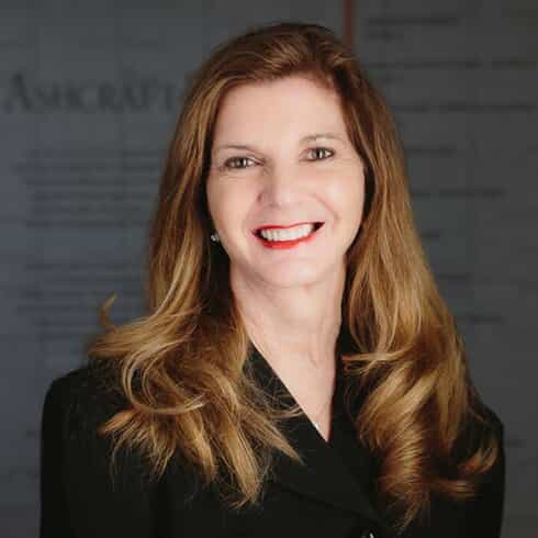 Professional headshot of Michelle Parfitt, Senior Partner, smiling, wearing a black blazer, in front of Ashcraft & Gerel sign