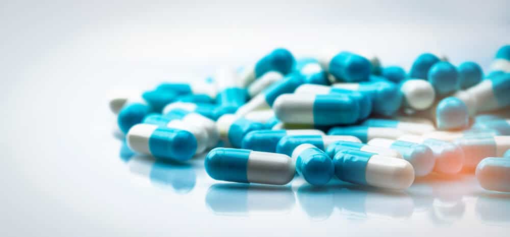 Pile of blue and white capsule pills on reflective surface.