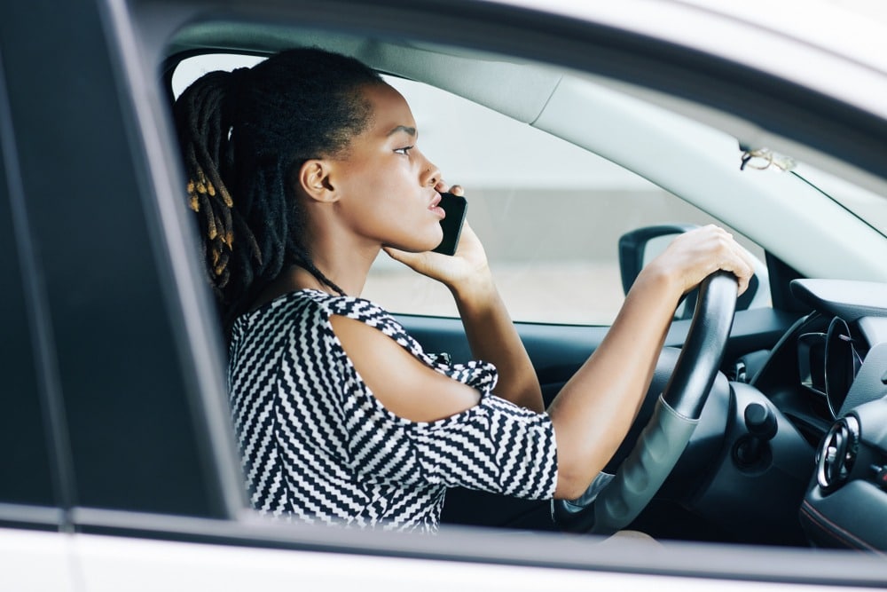 Woman driving car while talking on cell phone, hand on steering wheel.