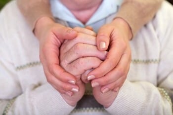 Close-up of hands clasped together, younger hands holding elderly hands.