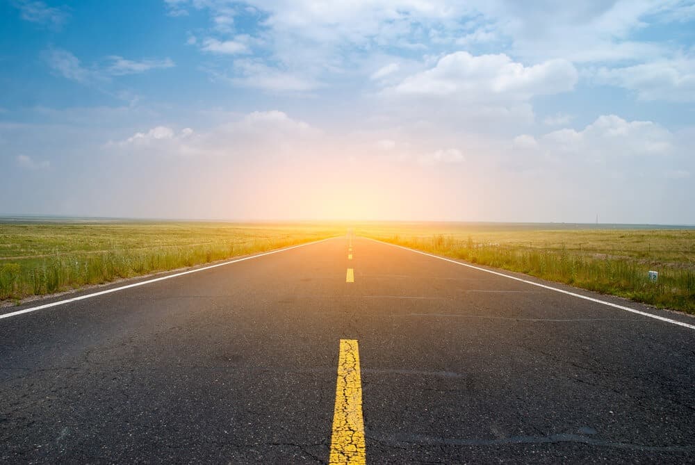 Empty rural highway stretching toward sunrise on horizon.