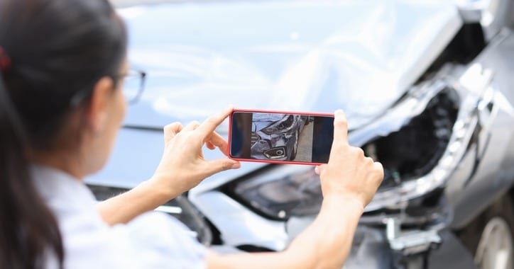 An astute woman taking a picture of damage to her car after a car accident