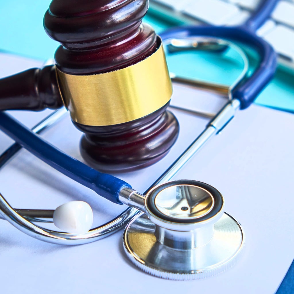 A gavel overtop a stethoscope on a gray table