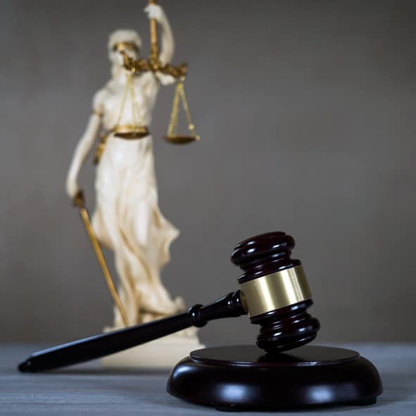 Wooden gavel on desk with Lady Justice statue blurred in background.
