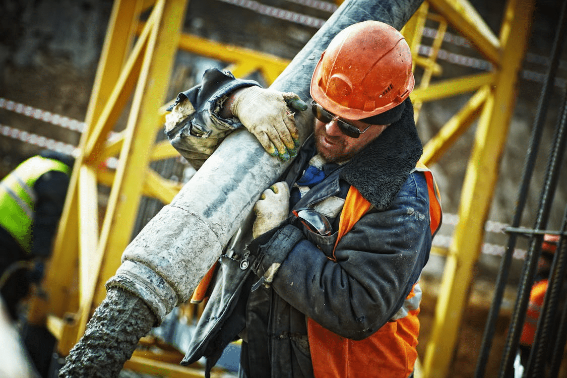 Construction worker in hard hat operating concrete pour hose at job site