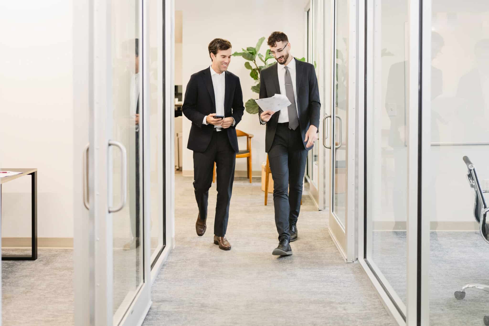 Dos abogados caminando y conversando por el pasillo de la oficina, revisando un documento