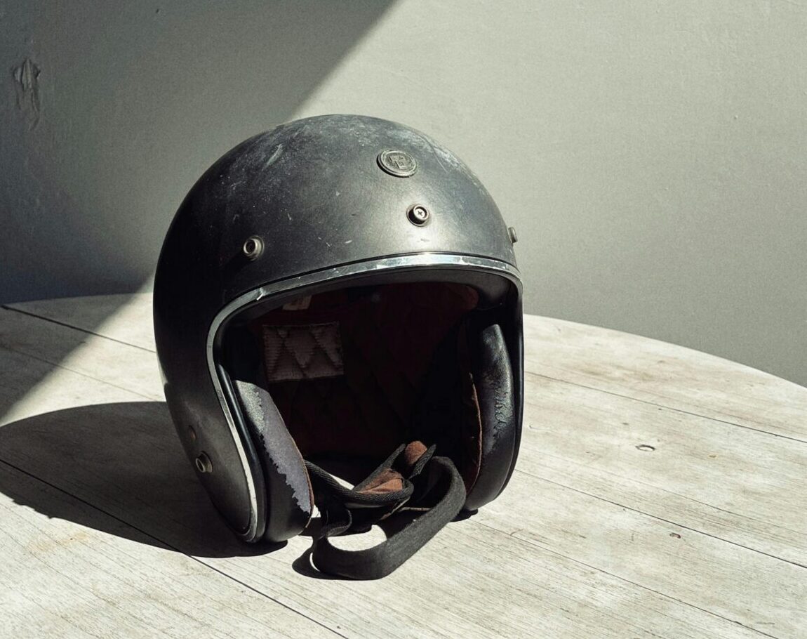 Worn black open-face motorcycle helmet on wood table