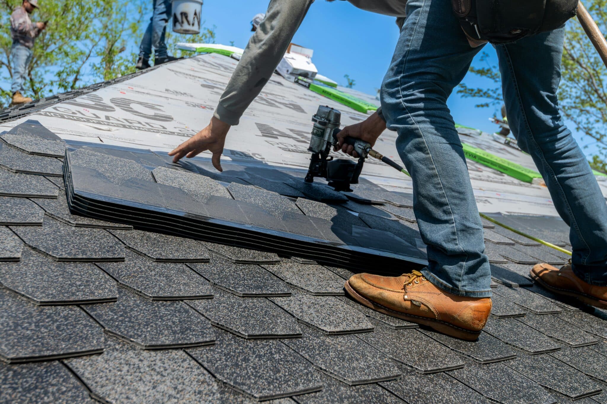 Roofers installing asphalt shingles with nail gun on new roof