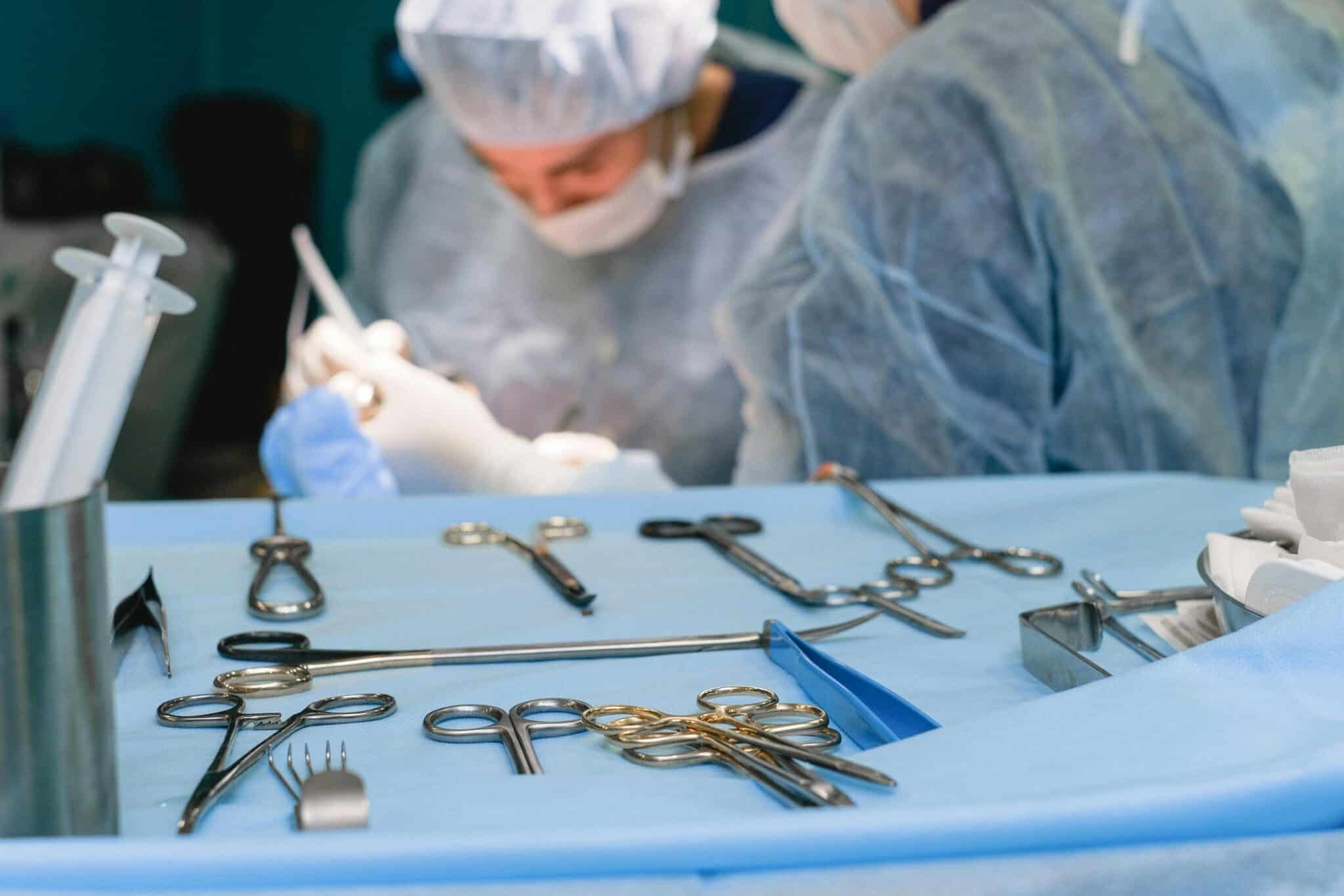 Surgical instruments laid out on tray, surgeons operating in background