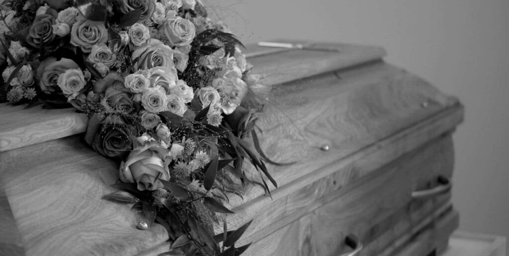 Rose bouquet draped across wooden casket, black and white photo.