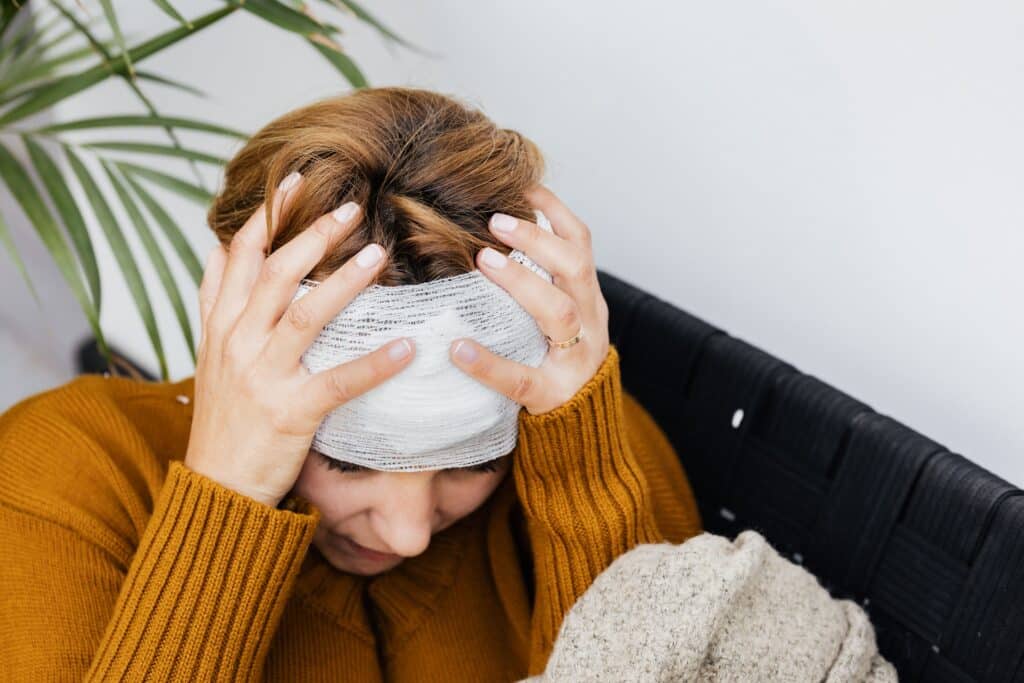Woman with bandaged head holding forehead in distress.