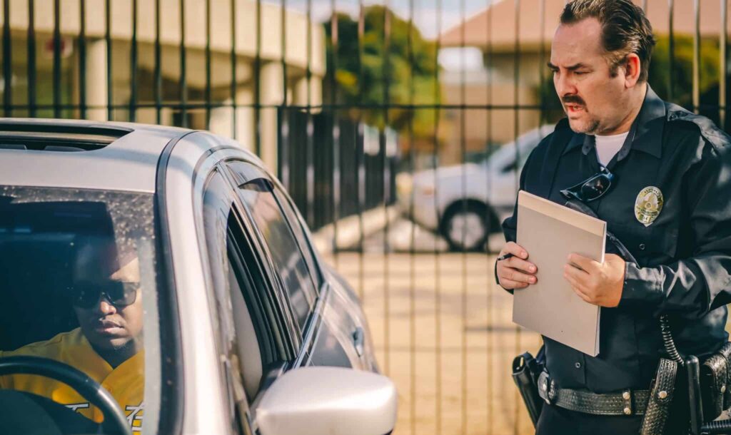 Police officer standing beside car window, speaking to driver during traffic stop.