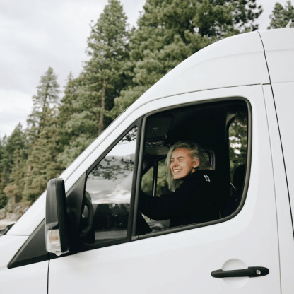 5099d80d7610719b63e1128f186452c58f33f1e0 Woman smiling in driver's seat of white van, forest in background