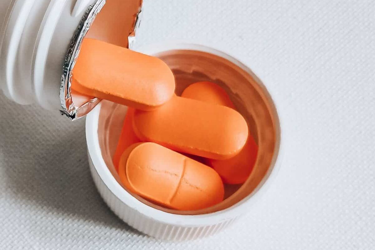 Cápsulas naranjas derramándose de un frasco de pastillas abierto con sello de aluminio